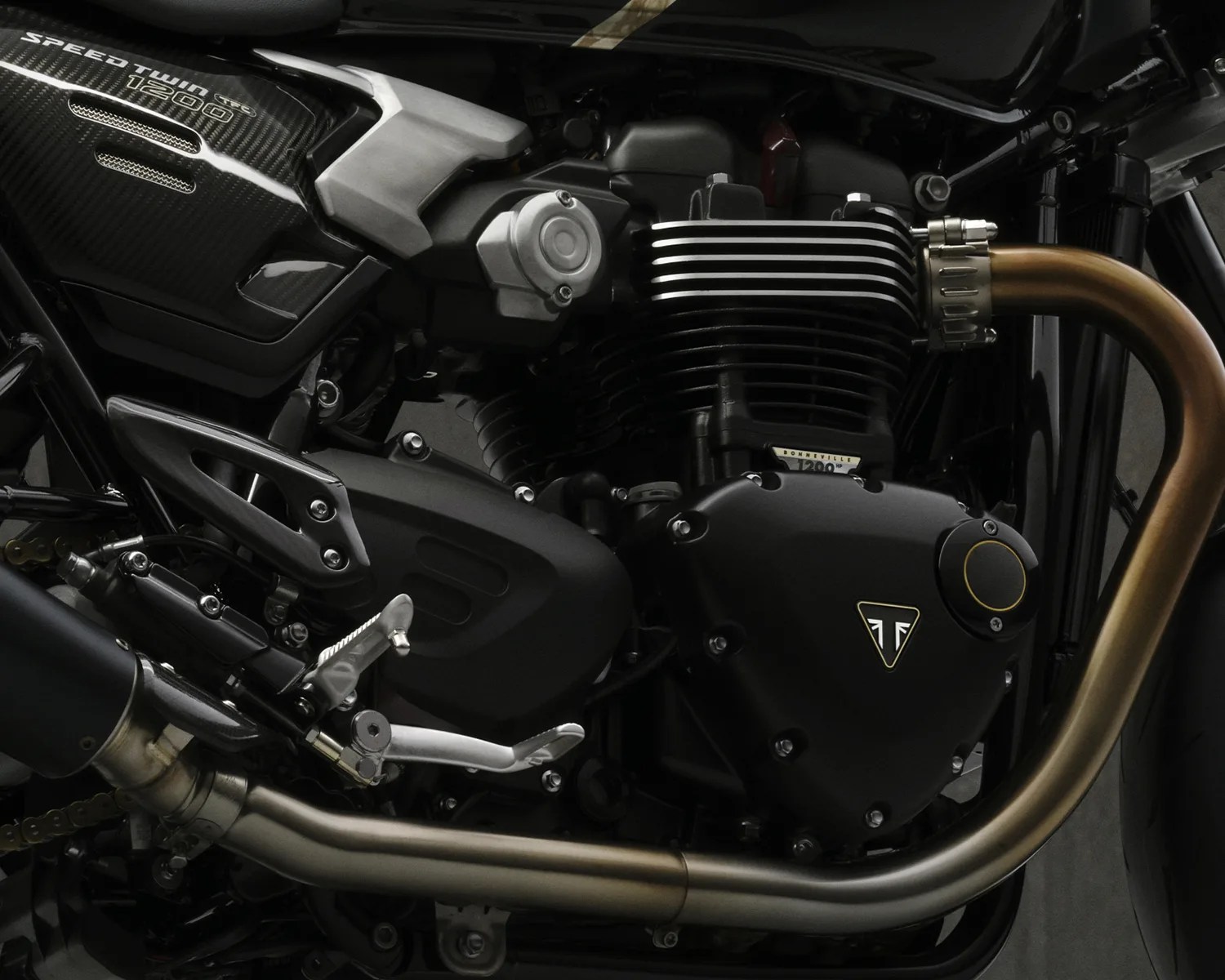 Close-up of a black Triumph Speed Twin 1200 motorcycle engine with bronze exhaust pipe.