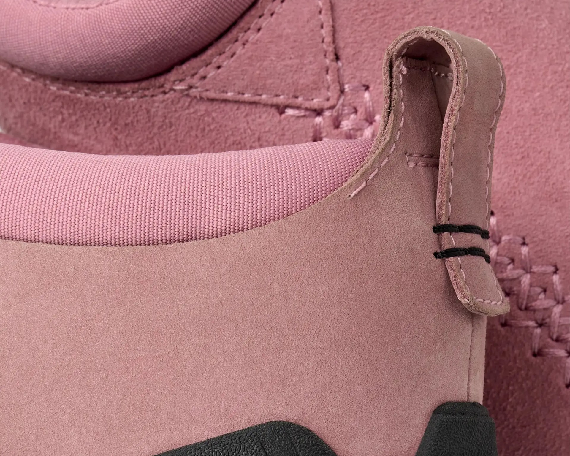 Close-up of pink suede shoe with fabric collar and stitched pull tab.