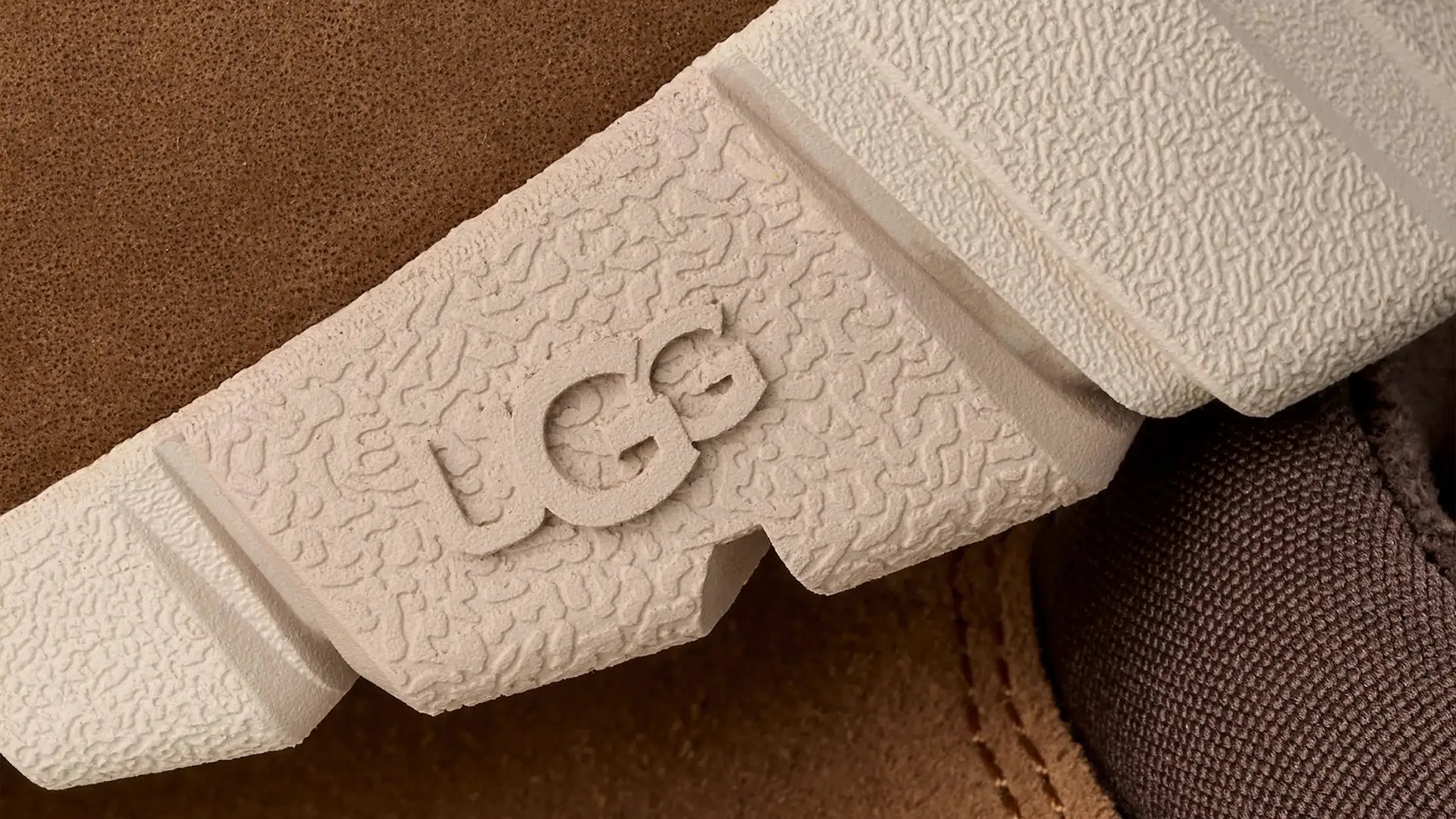 Close-up of a beige textured shoe sole with the embossed "GG" logo on a brown fabric and leather background.