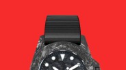 Black marbled watch case with black dial and round white markers, paired with a black ribbed strap on a red background.