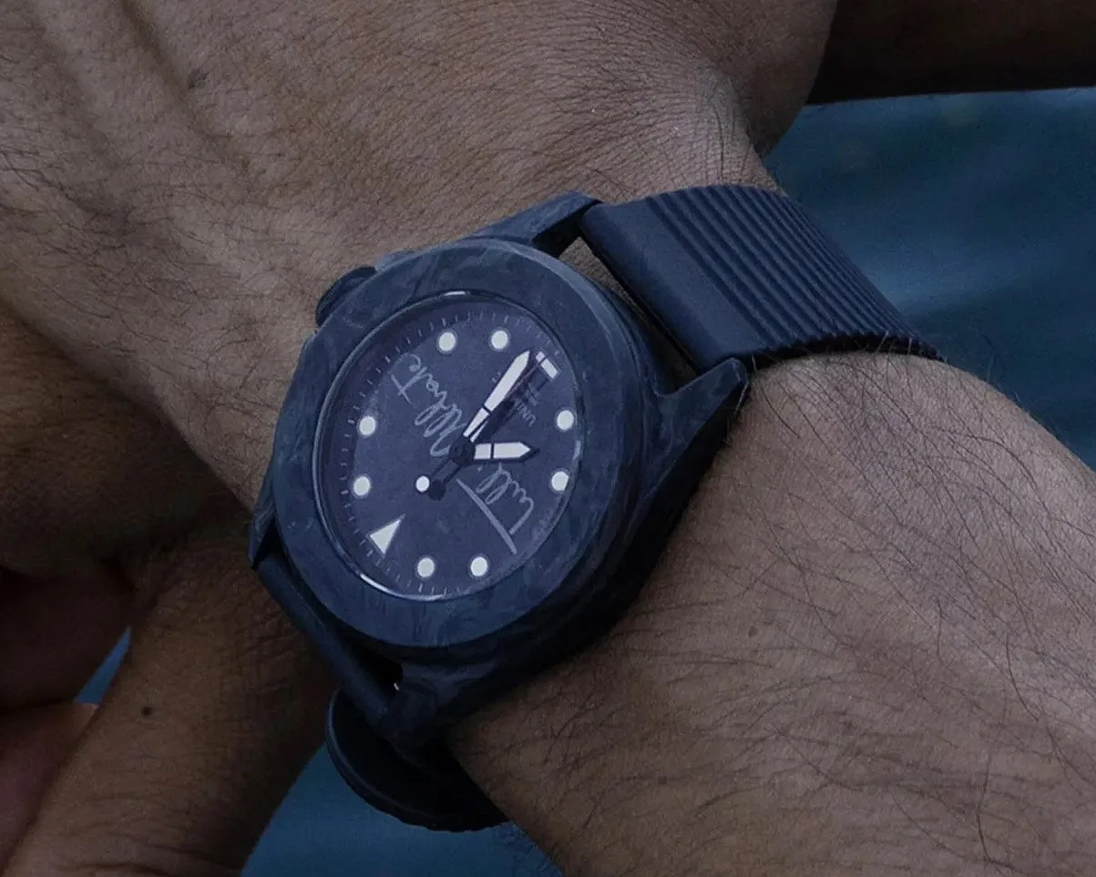 Black wristwatch with a textured dial and white hour markers worn on a person's wrist.