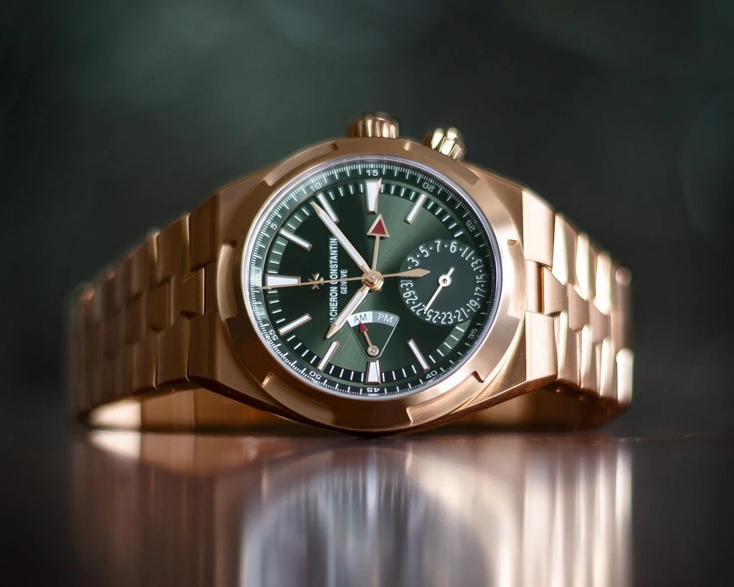 Rose gold wristwatch with green dial, date subdial, and AM/PM indicator on a reflective surface.