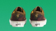 Pair of brown and green camouflage Vans sneakers shown from the back on a green background.