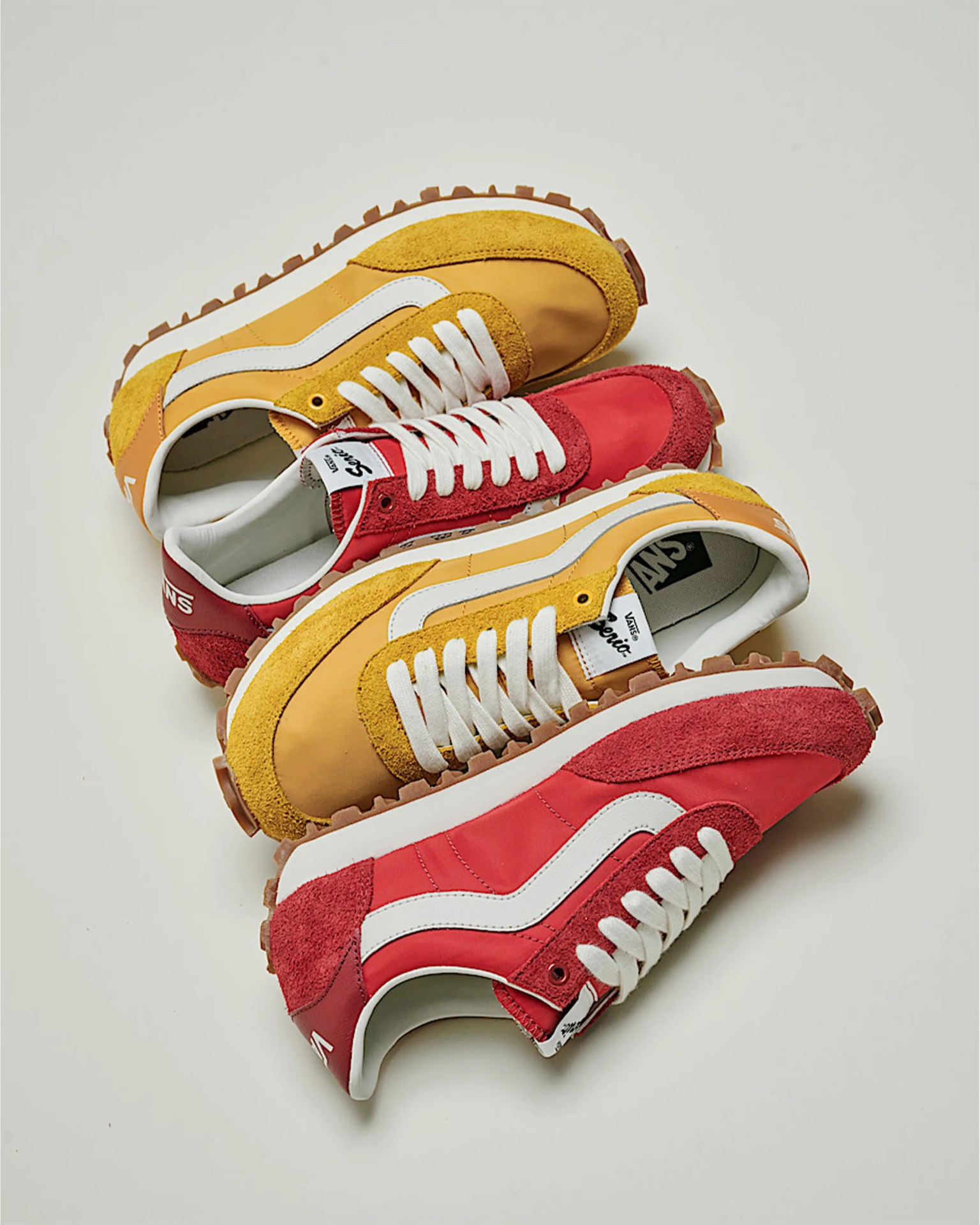Pair of Vans sneakers with yellow and red suede and nylon uppers, white laces, and gum rubber soles on a white background.