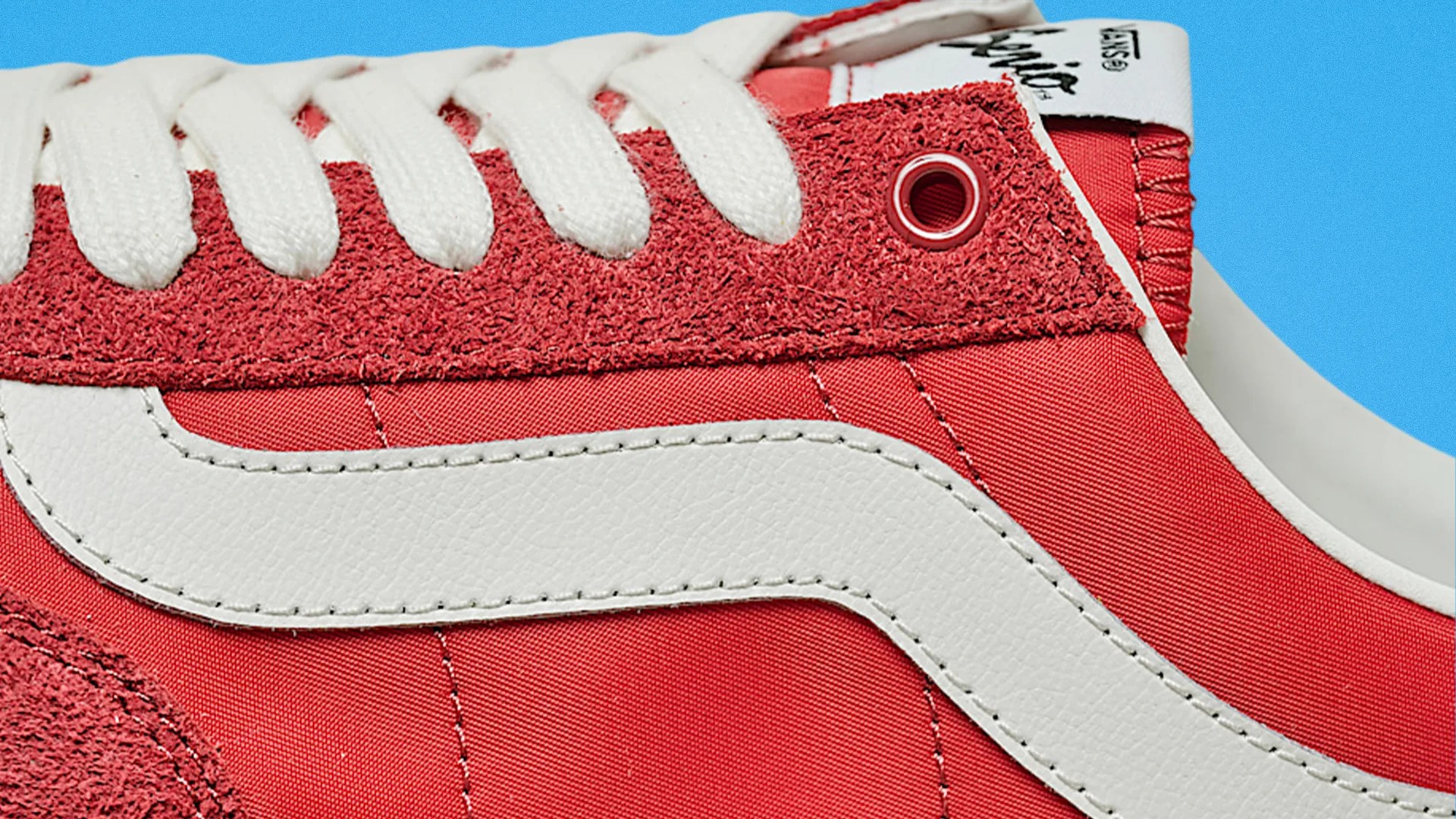 Close-up of a red sneaker with white laces and a white leather stripe on the side against a blue background.