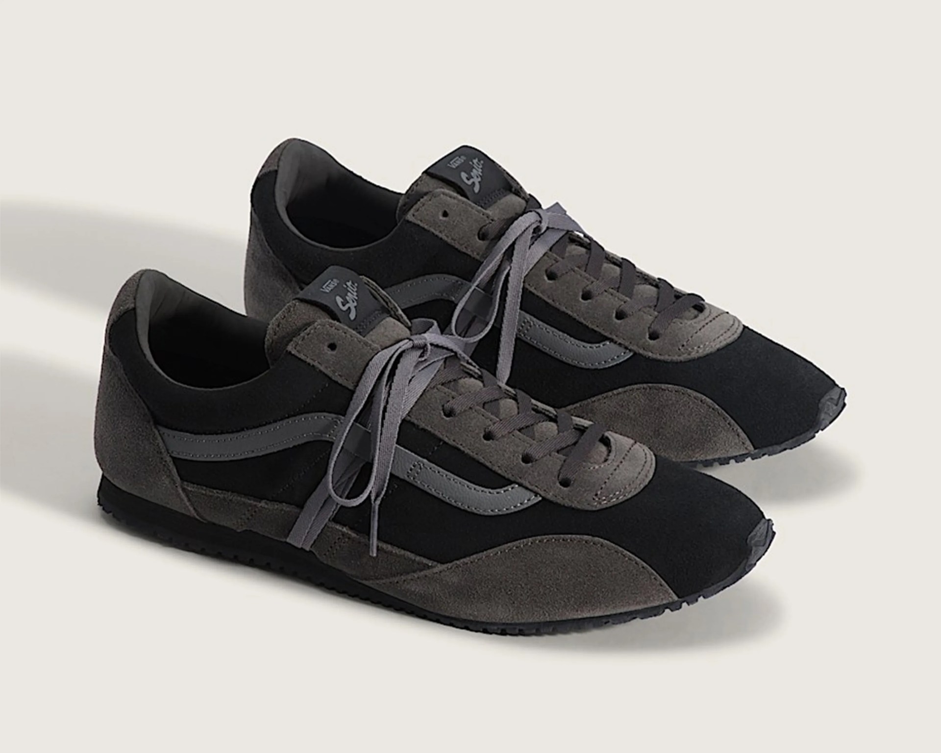 Pair of black and gray Vans Suede sneakers with gray laces on a light background.