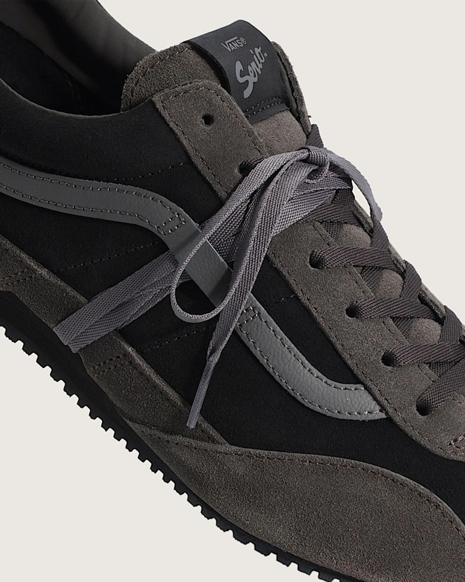 Close-up of a black and dark gray Vans sneaker with suede and leather materials and gray laces.