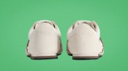 Pair of beige suede sneakers shown from the back on a green background.