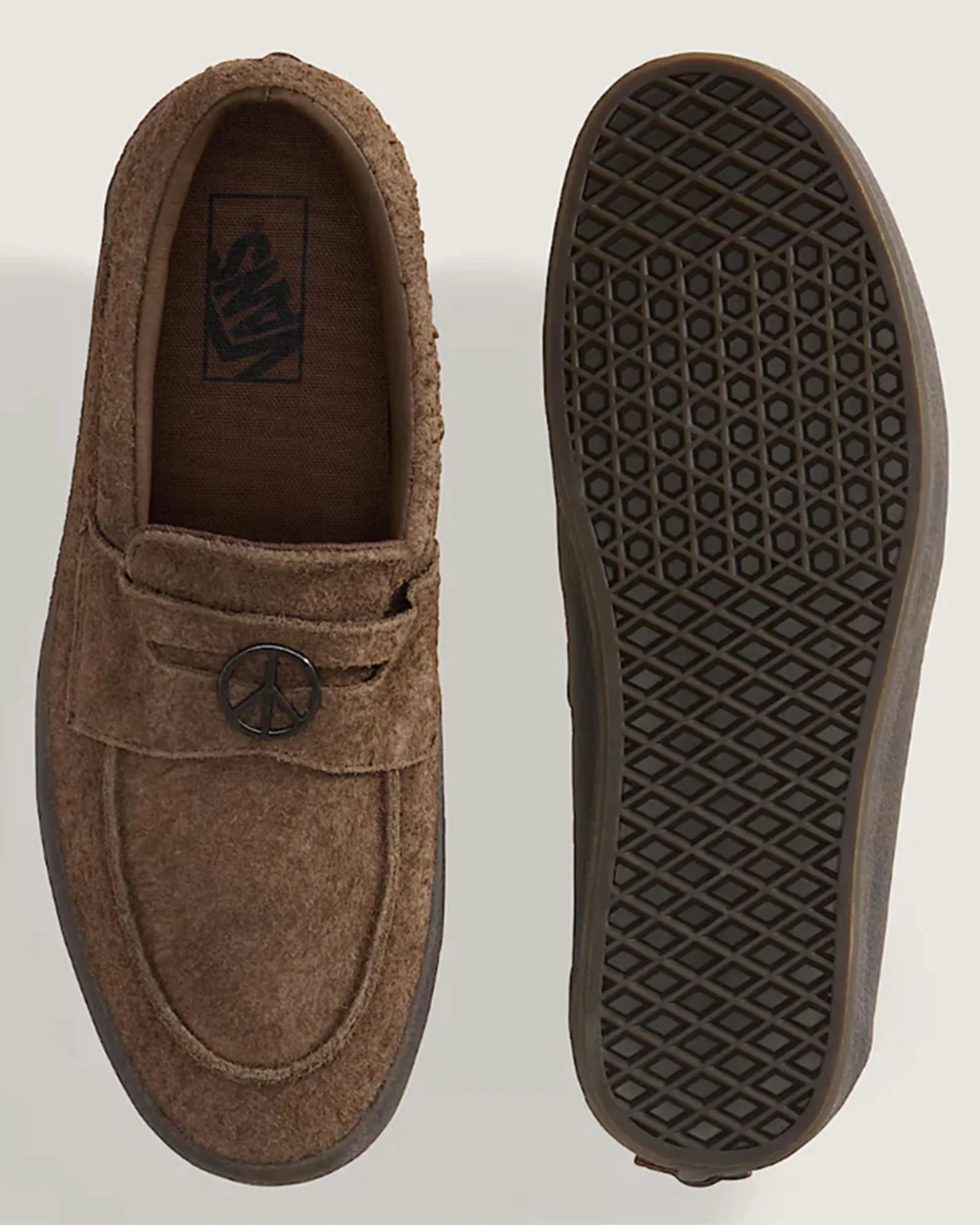 Brown suede slip-on shoe with peace sign metal detail and patterned rubber sole.
