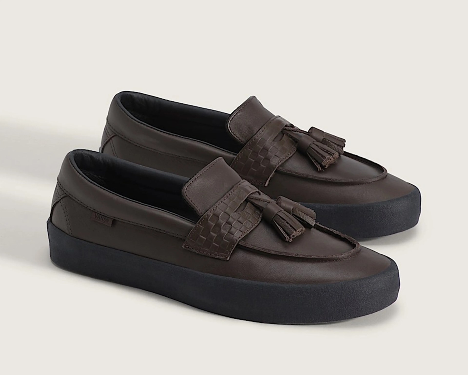 Pair of dark brown leather loafers with tassels and black rubber soles on a light surface.