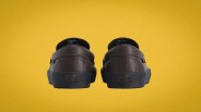 Pair of brown Vans leather sneakers with black soles shown from the back on a yellow background.