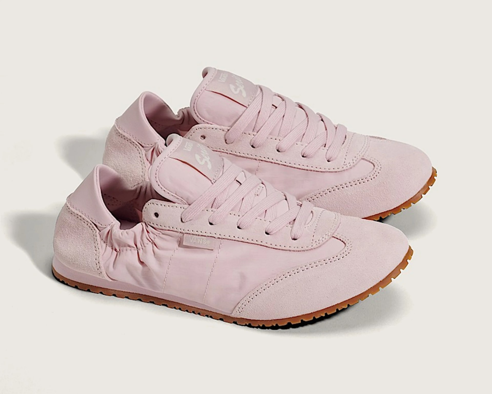 Pair of light pink Vans sneakers with suede accents and gum rubber soles on a white background.