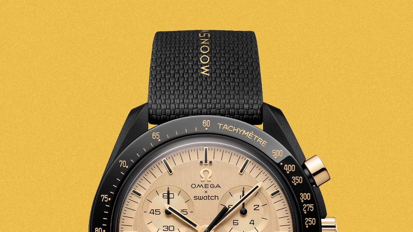 Black and gold Omega x Swatch wristwatch with tachymeter bezel and black textured strap on a yellow background.