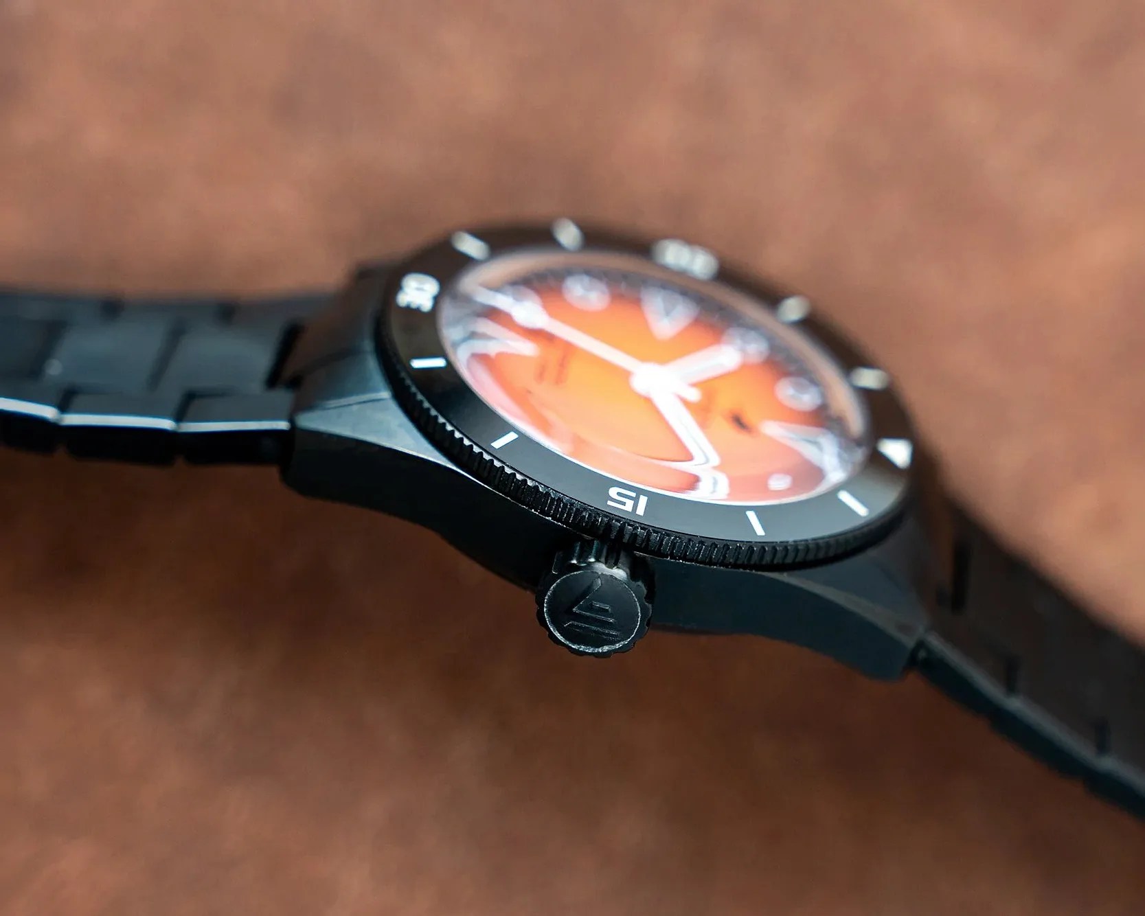 Black wristwatch with orange dial and white markings on a brown surface.