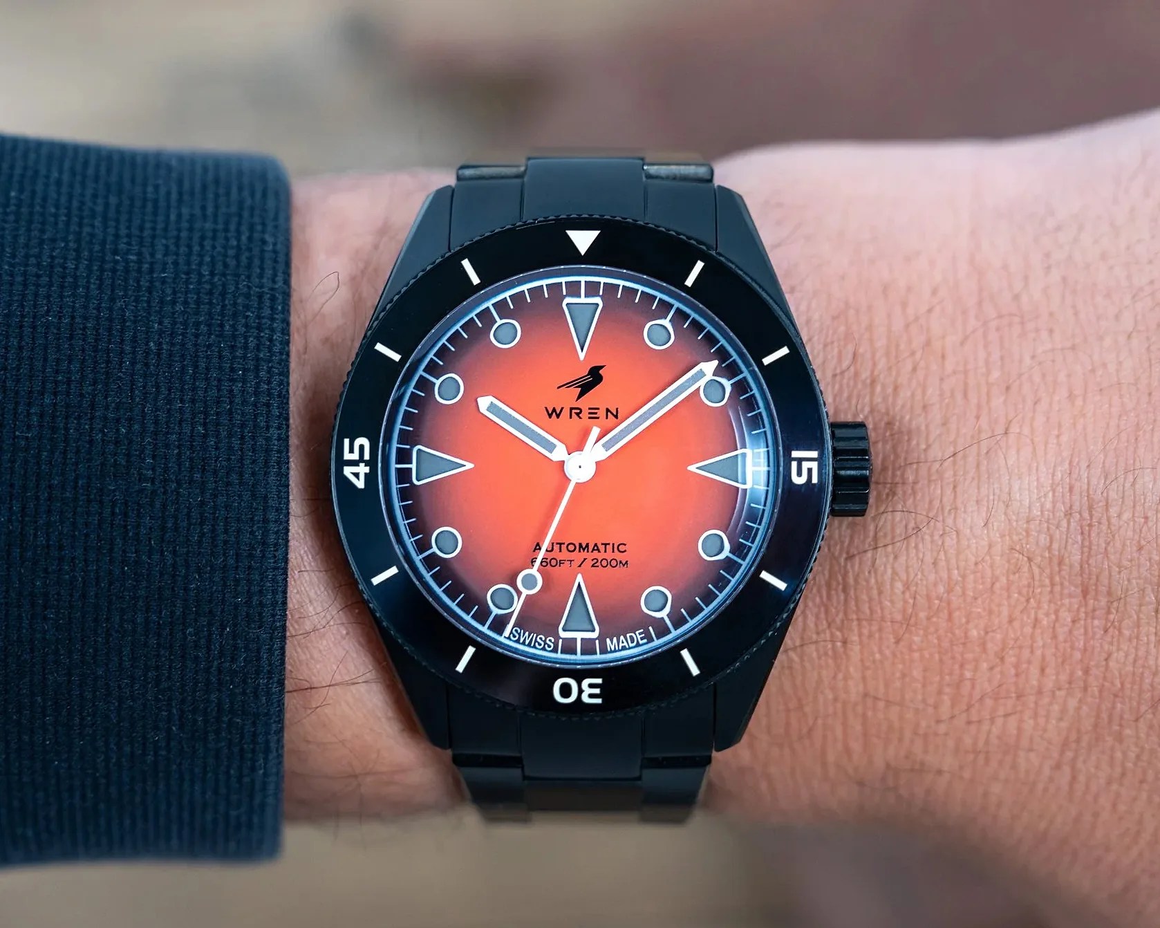 Black metal wristwatch with orange gradient dial and white markers worn on a wrist.