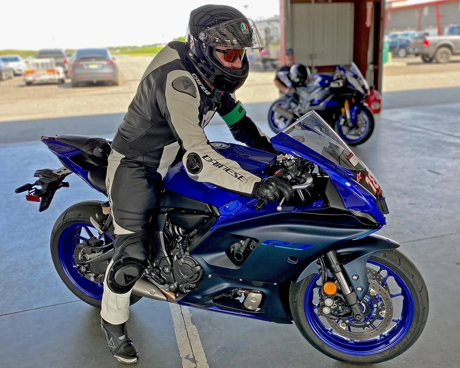 Person in black and white Dainese motorcycle gear sitting on a blue Yamaha R7 sportbike inside a garage.