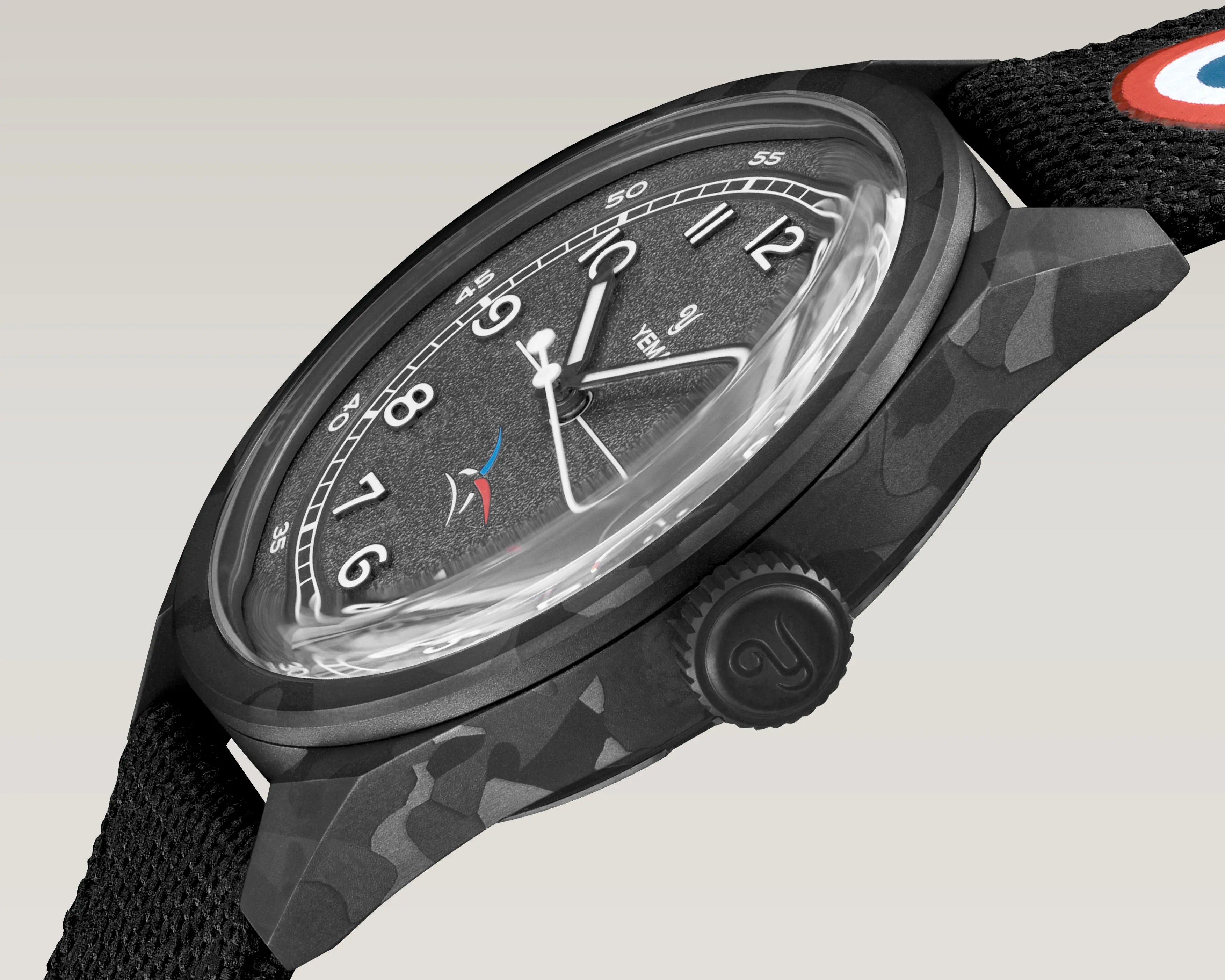 Close-up of a black textured dial wristwatch with white numerals, black camouflage case, and black fabric strap with a red, white, and blue roundel.