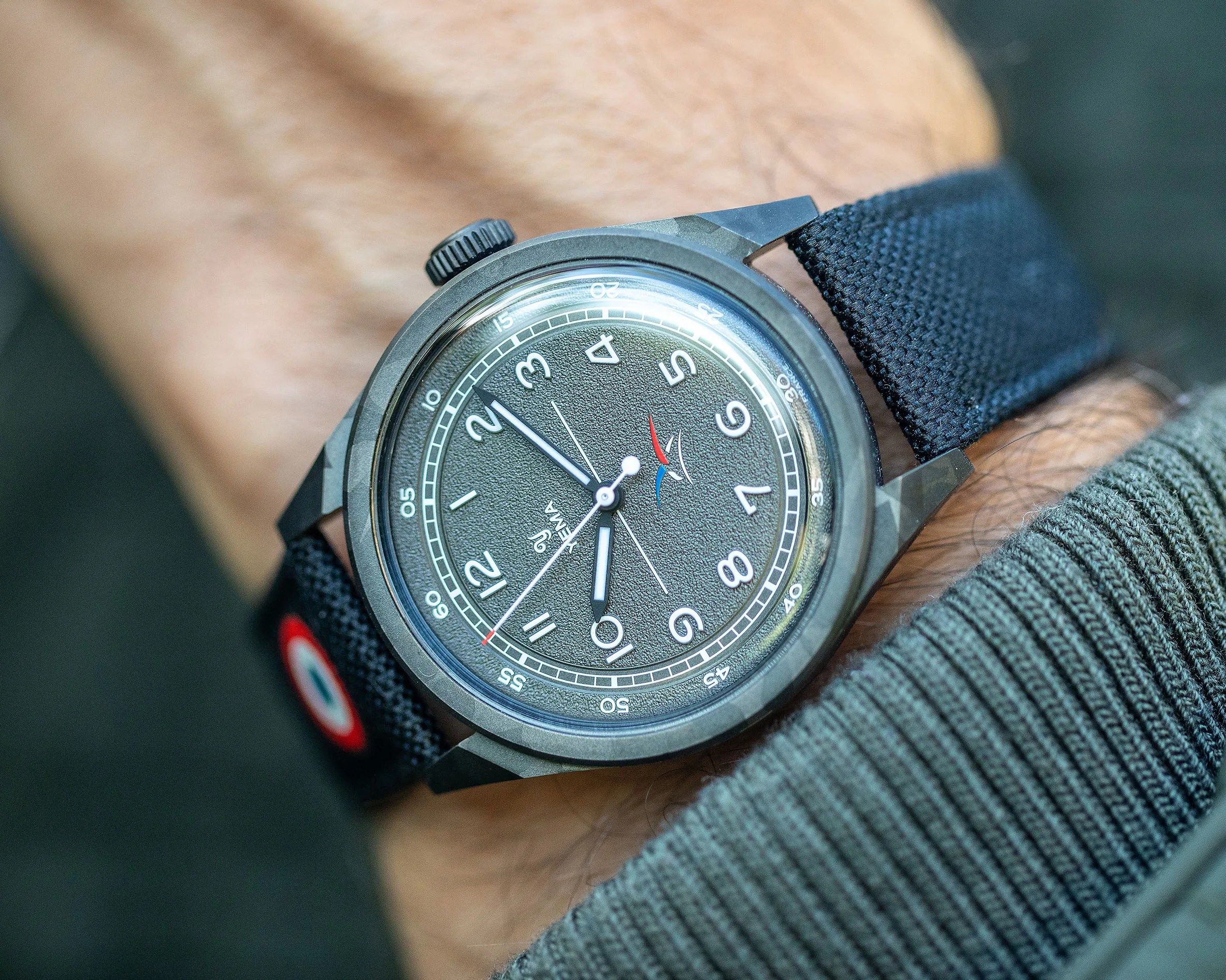 Black textured dial wristwatch with white numerals and black fabric strap worn on wrist.