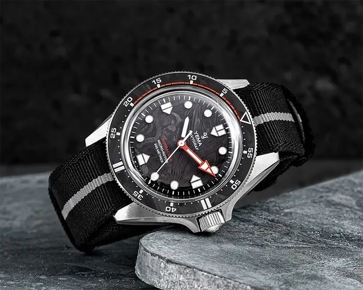 Silver Yema dive watch with black textured dial, red and white hands, and black fabric strap with gray stripe.