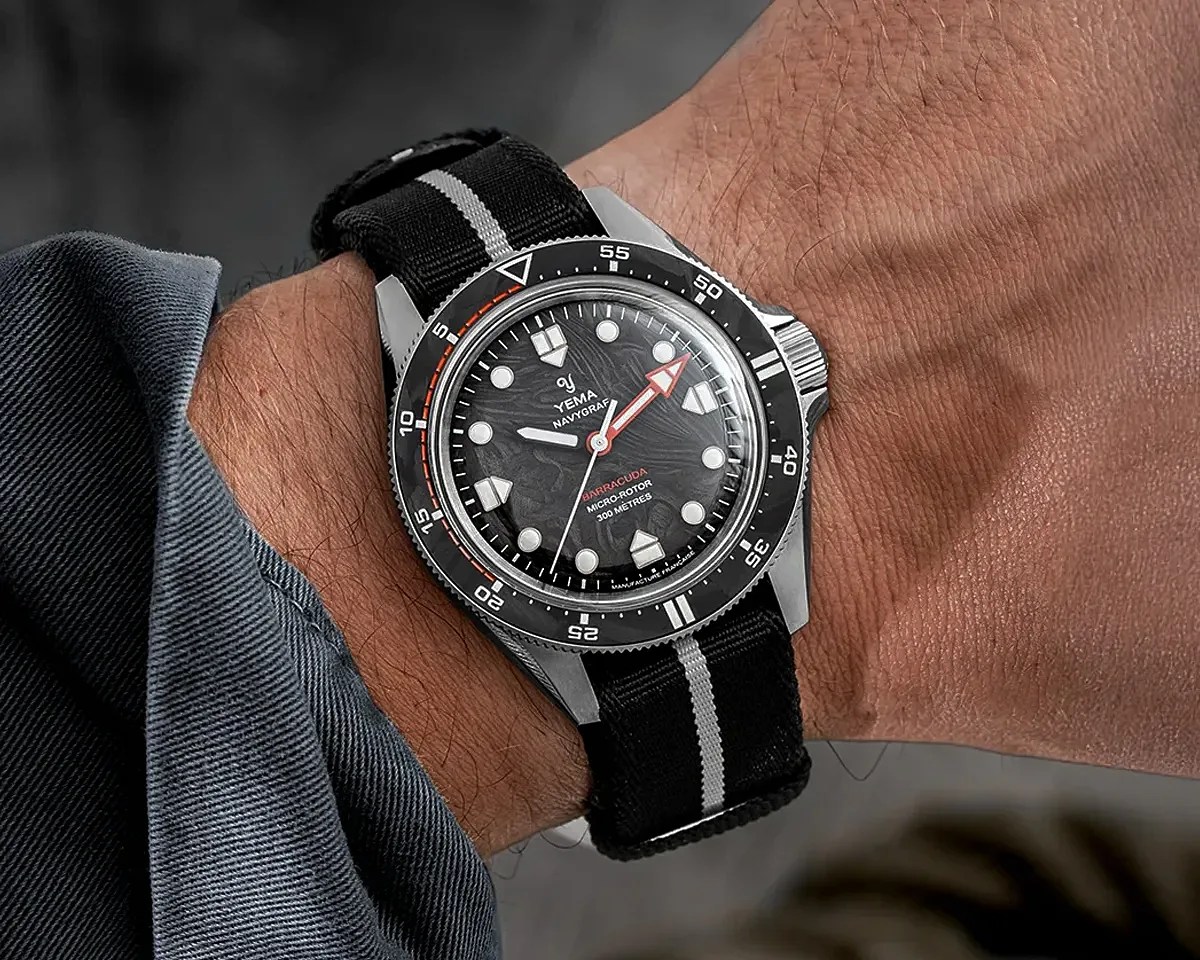 Black Yema Navygraf Barracuda wristwatch with a textured dial and black fabric strap with a gray stripe worn on a wrist.