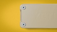 Beige YETI cooler corner with visible screws on a textured gold background.