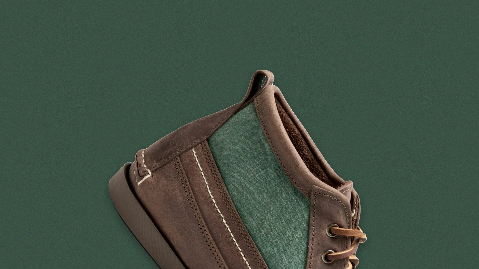 Brown leather and green fabric shoe with beige stitching on a dark green background.