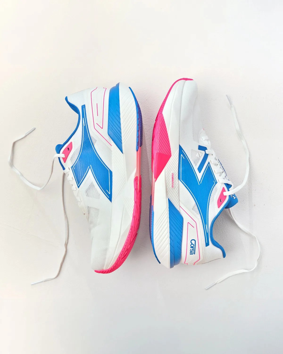 Pair of white athletic shoes with blue and pink accents and white laces on a white background.