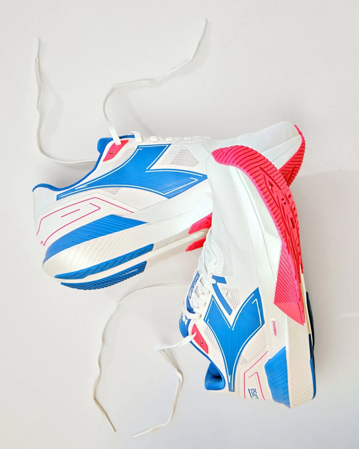 Pair of white athletic shoes with blue and pink accents and white laces on a white surface.