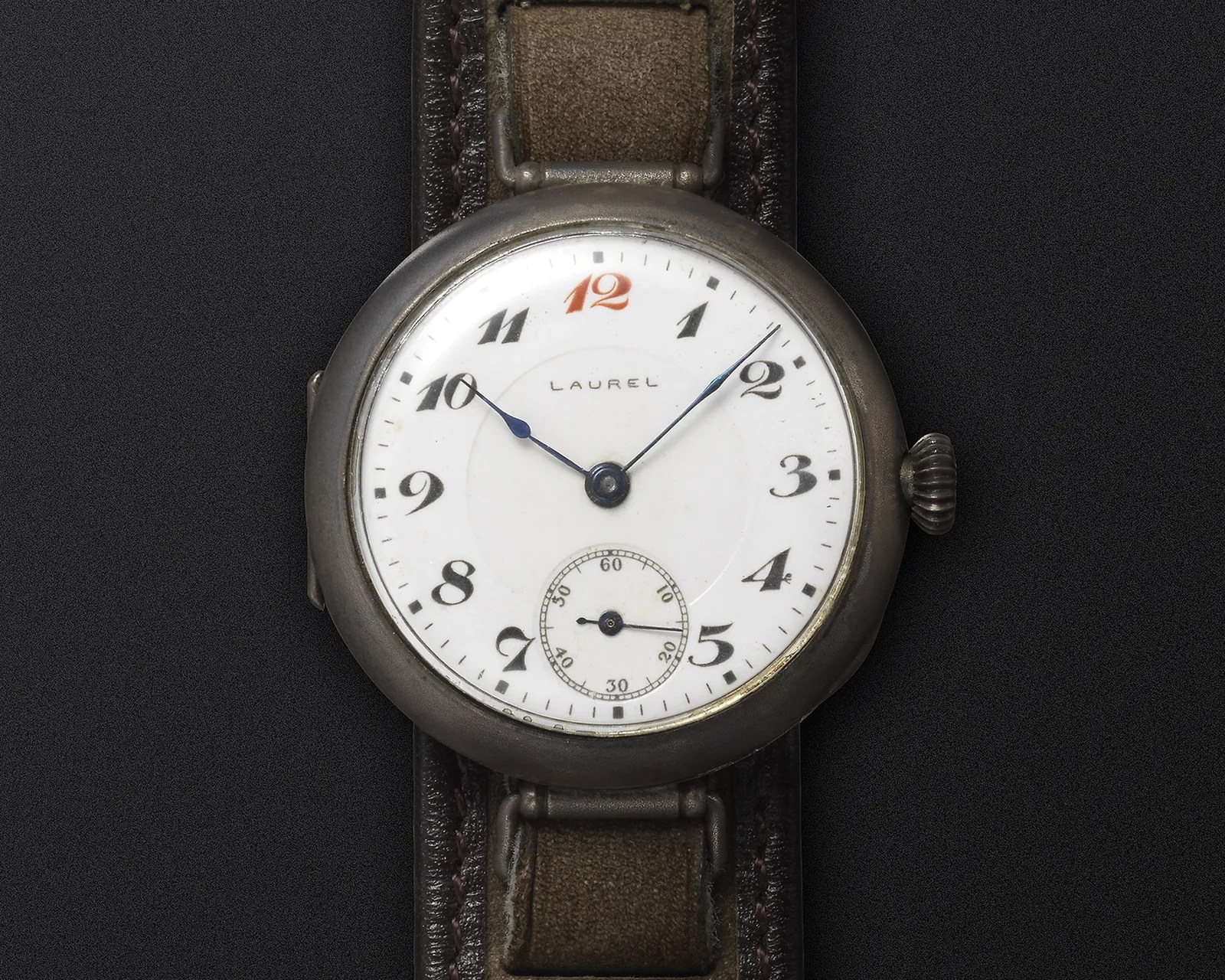 Vintage Laurel wristwatch with white dial, black numerals, red 12, and brown leather strap on black background.