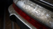 Rear end of a dirty silver Porsche Carrera RS with a red taillight.