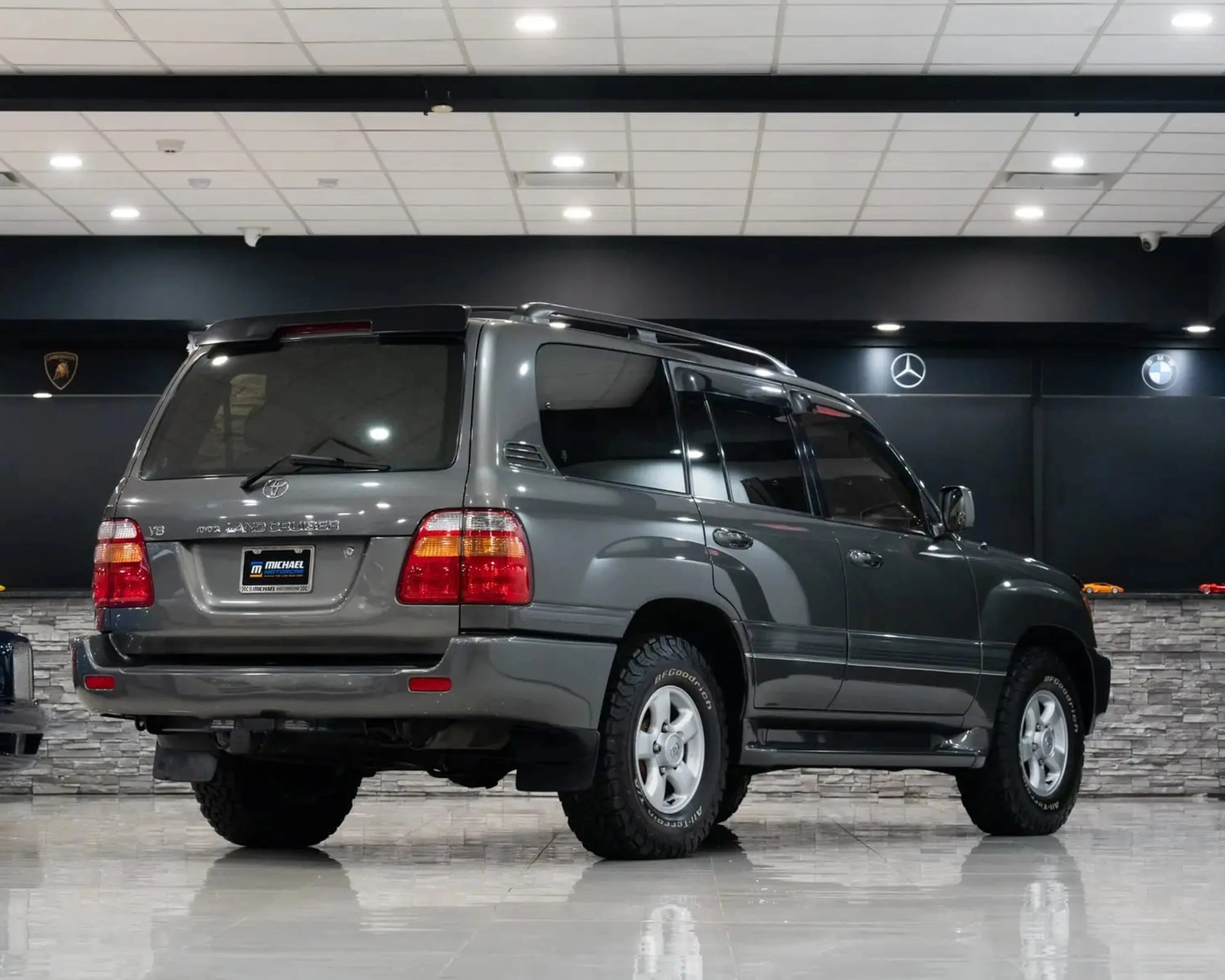 Gray Toyota Land Cruiser SUV with off-road tires parked indoors on a shiny tiled floor.