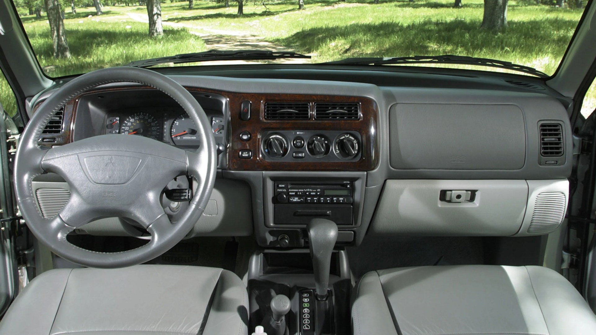 Gray leather steering wheel and seats with wood trim dashboard and automatic gear shift in a car interior.