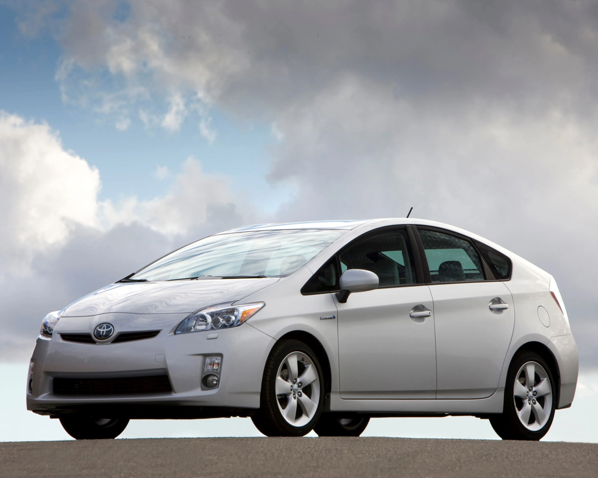 White Toyota Prius hybrid car parked on asphalt under a cloudy sky.