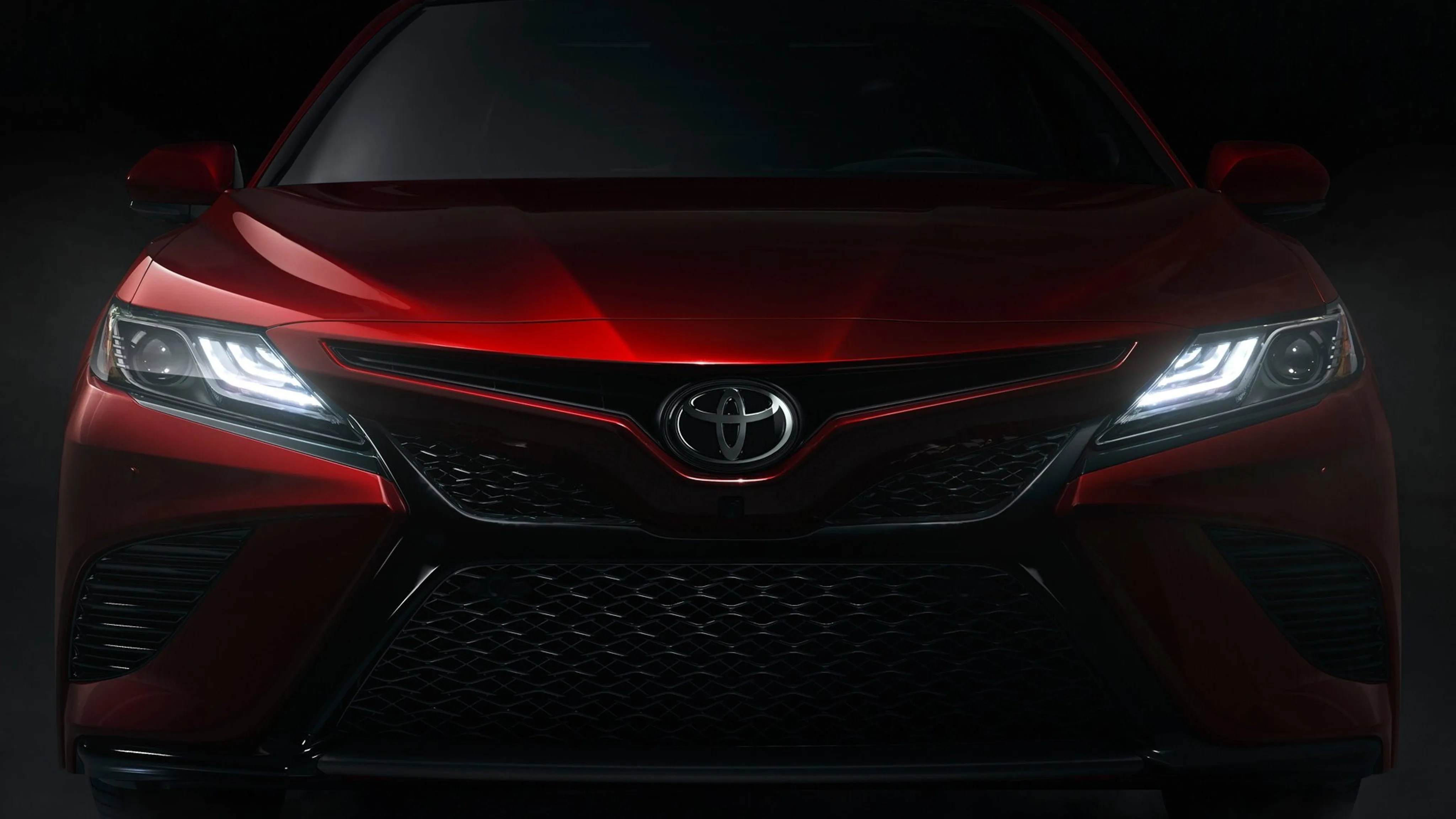 Front view of a red Toyota car with illuminated LED headlights in a dark setting.
