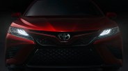 Front view of a red Toyota car with illuminated LED headlights in a dark setting.