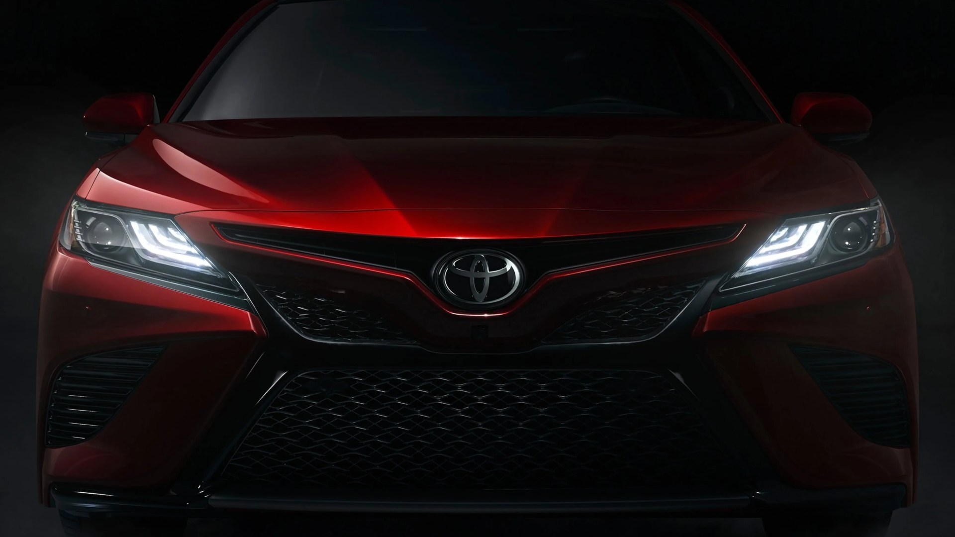Front view of a red Toyota car with illuminated LED headlights in a dark setting.