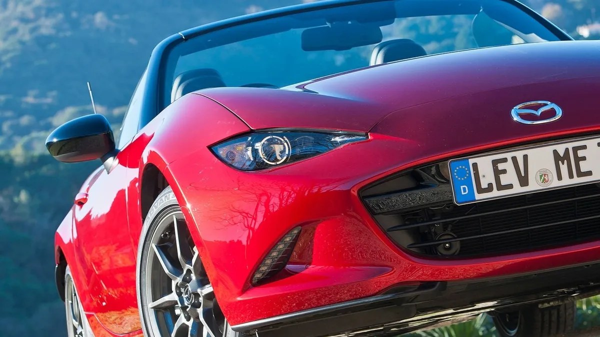 Red Mazda convertible sports car front with visible headlight, grille, and license plate.