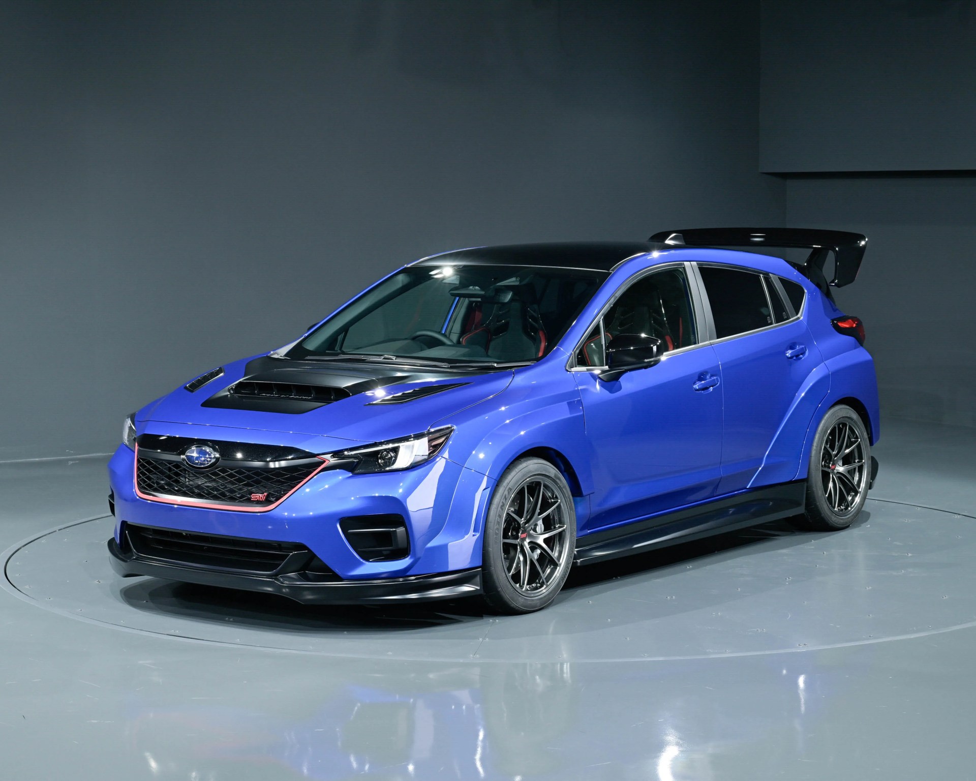 Blue Subaru WRX STI hatchback with black roof, hood scoop, large rear spoiler, and sporty alloy wheels in a studio.