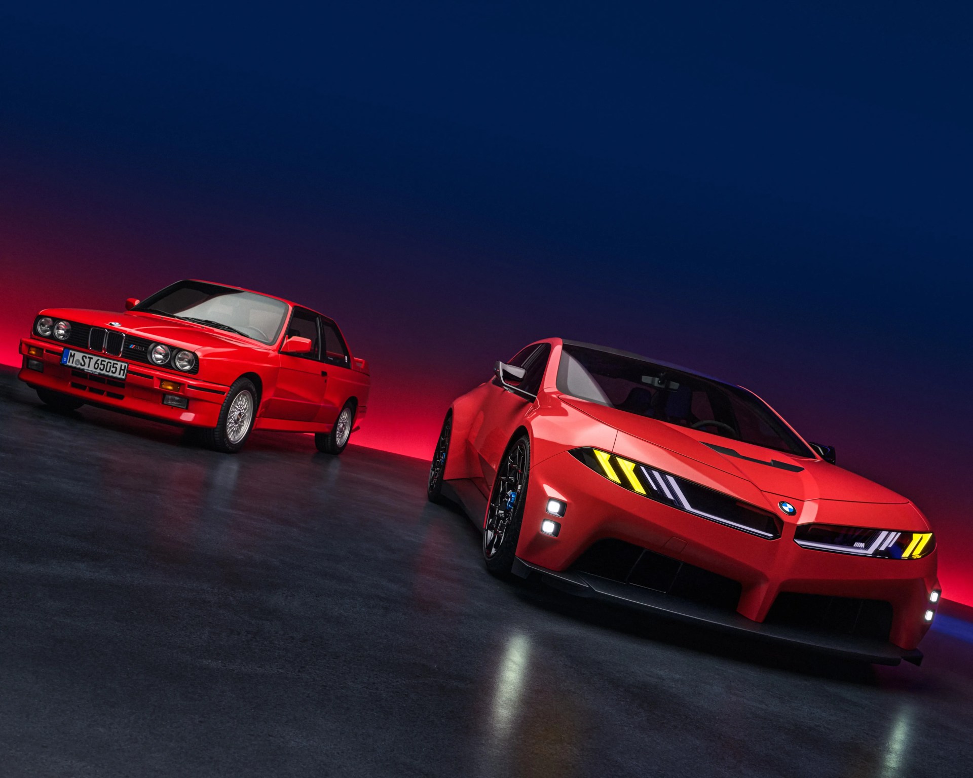 Two red BMW cars, one classic model and one modern model, parked on a dark reflective floor with a gradient blue to red background.