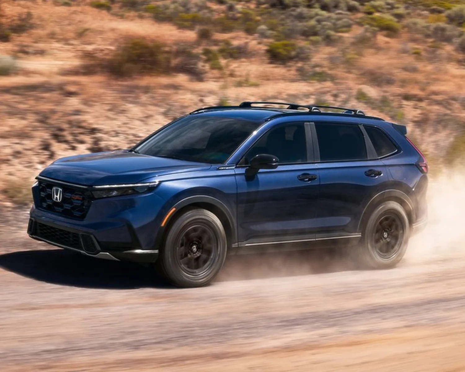 Blue Honda SUV driving on a dusty dirt road with black wheels and roof rails.