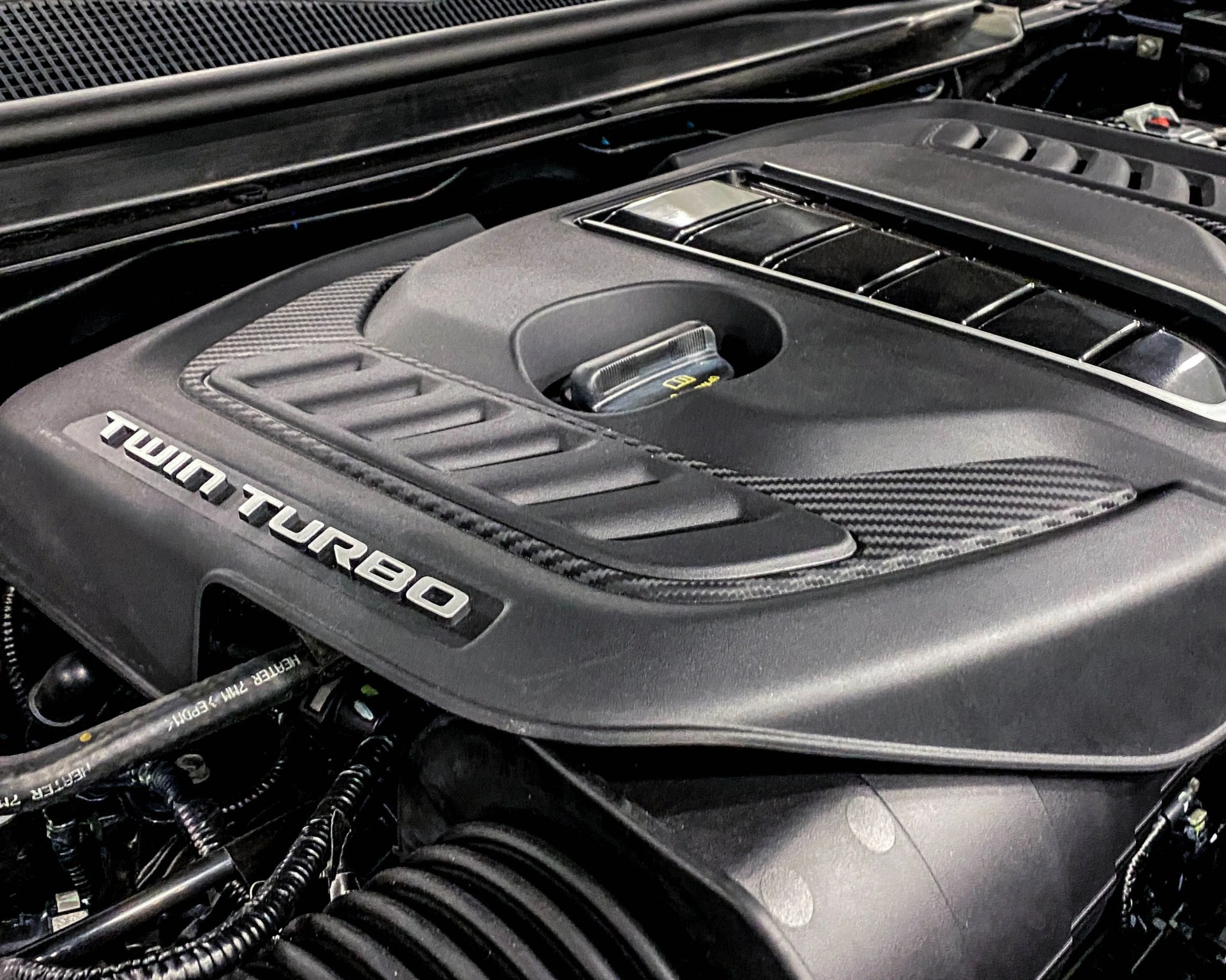Black engine cover with "Twin Turbo" lettering and carbon fiber accents inside a car engine bay.