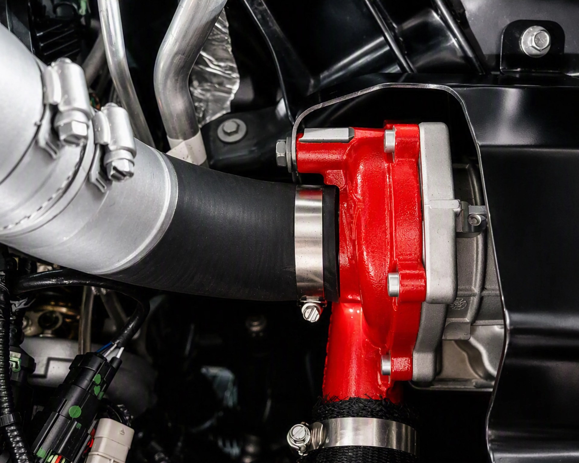 Close-up of a red metal engine component connected to black and silver hoses with metal clamps.