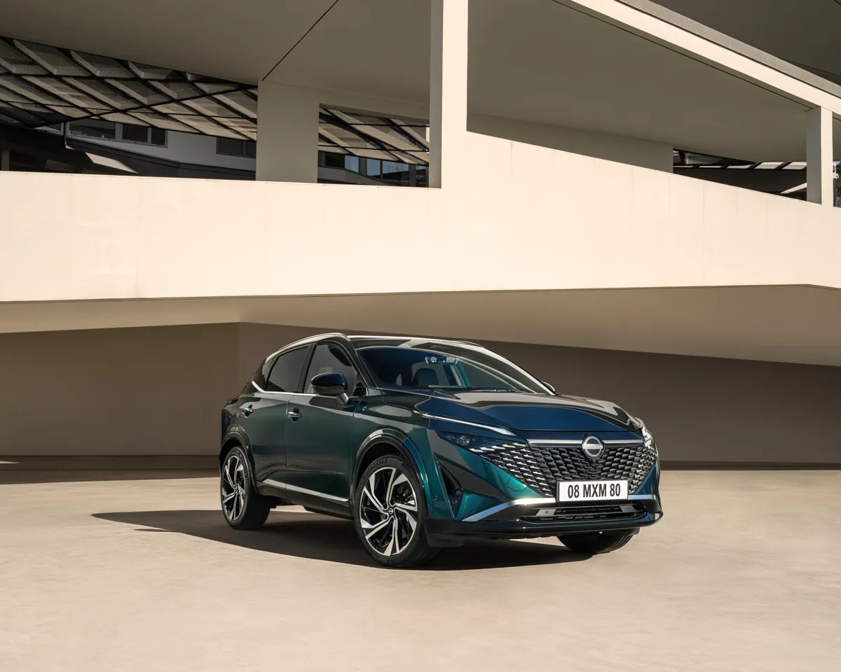 Dark green Nissan SUV with black roof and alloy wheels parked in front of a modern beige building.