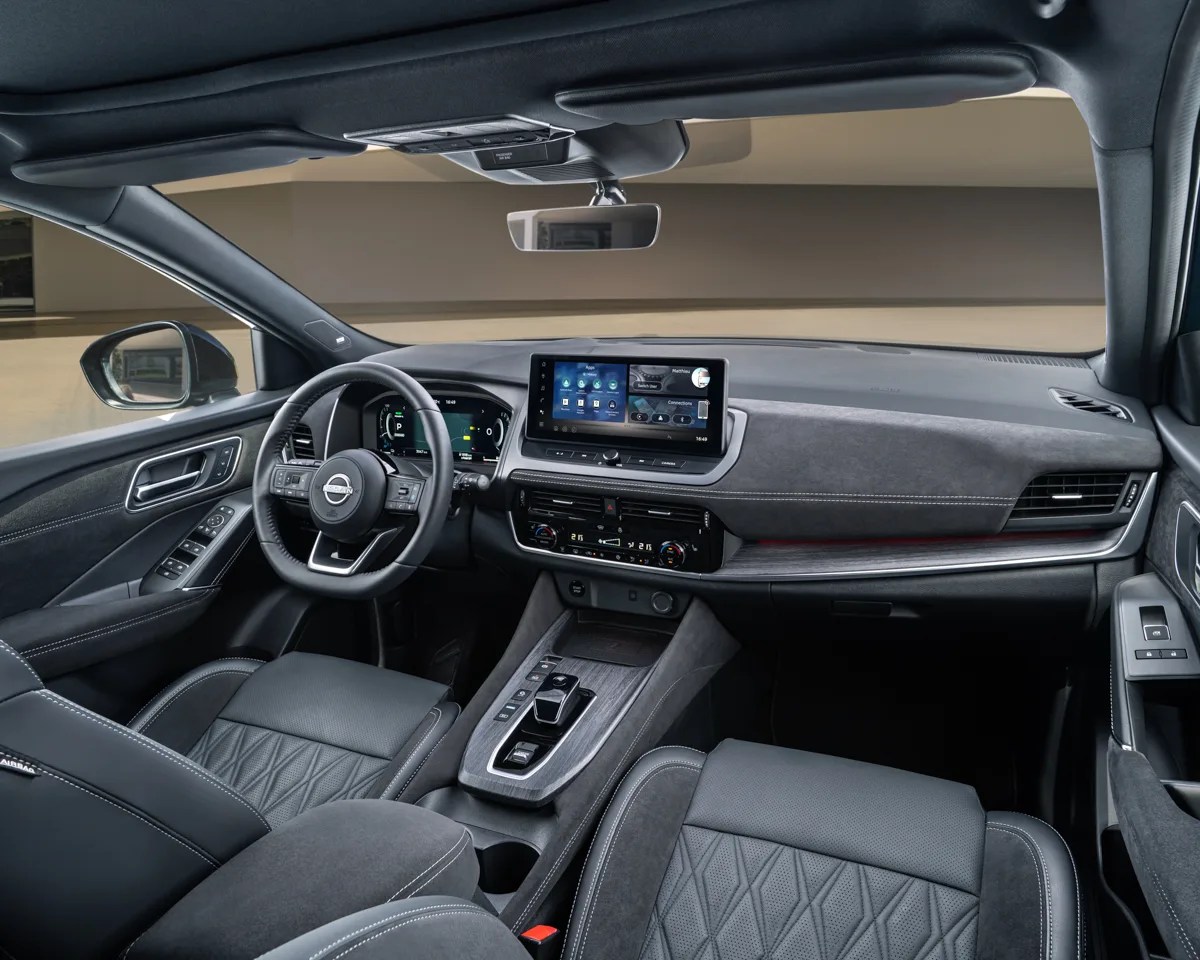 Black and gray Nissan car interior with digital dashboard, touchscreen display, and quilted leather seats.