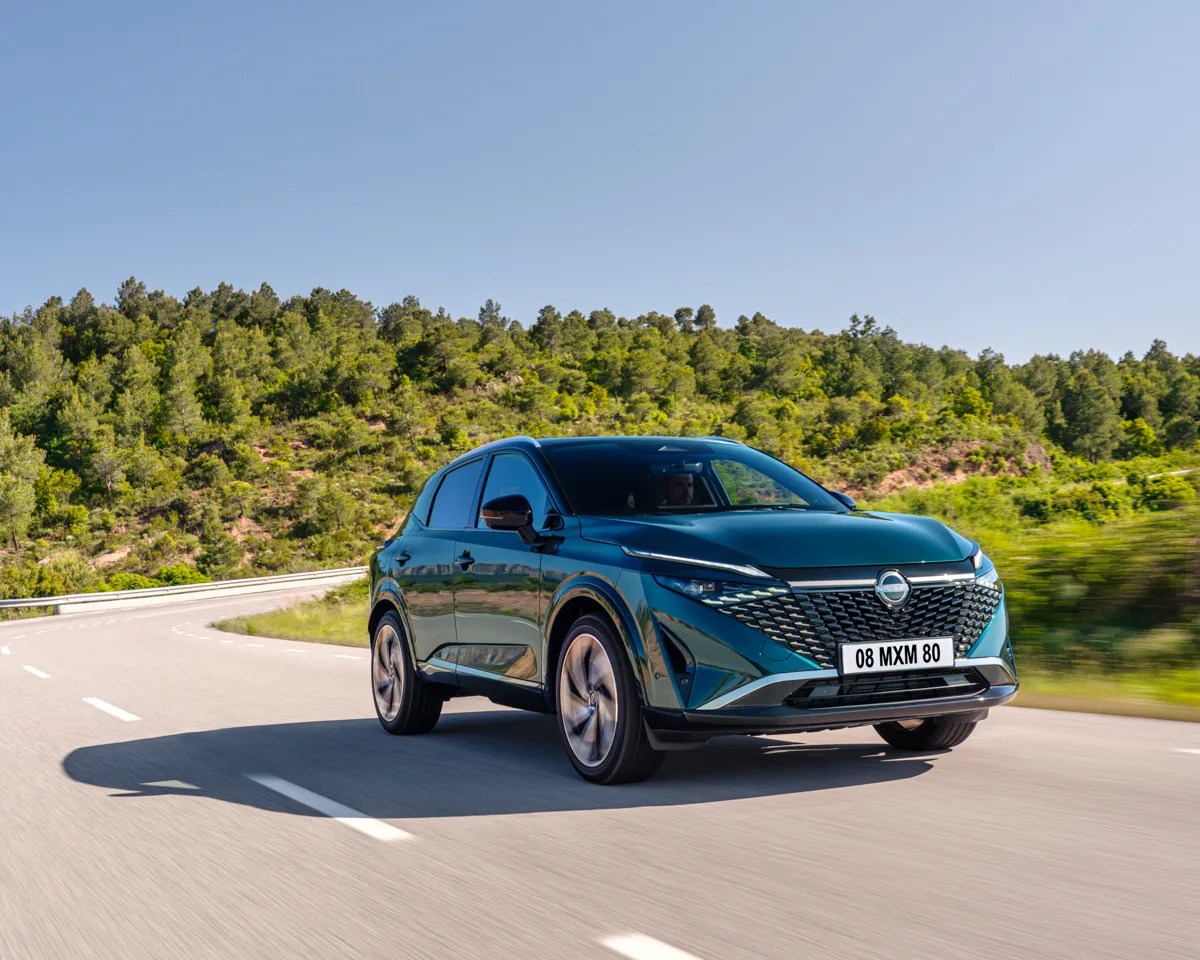 Dark green Nissan SUV driving on a curved road with trees and clear sky in the background.