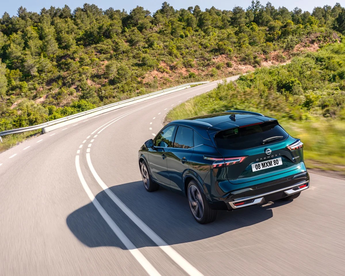 Dark green Nissan Qashqai SUV driving on a curved road with greenery on both sides.