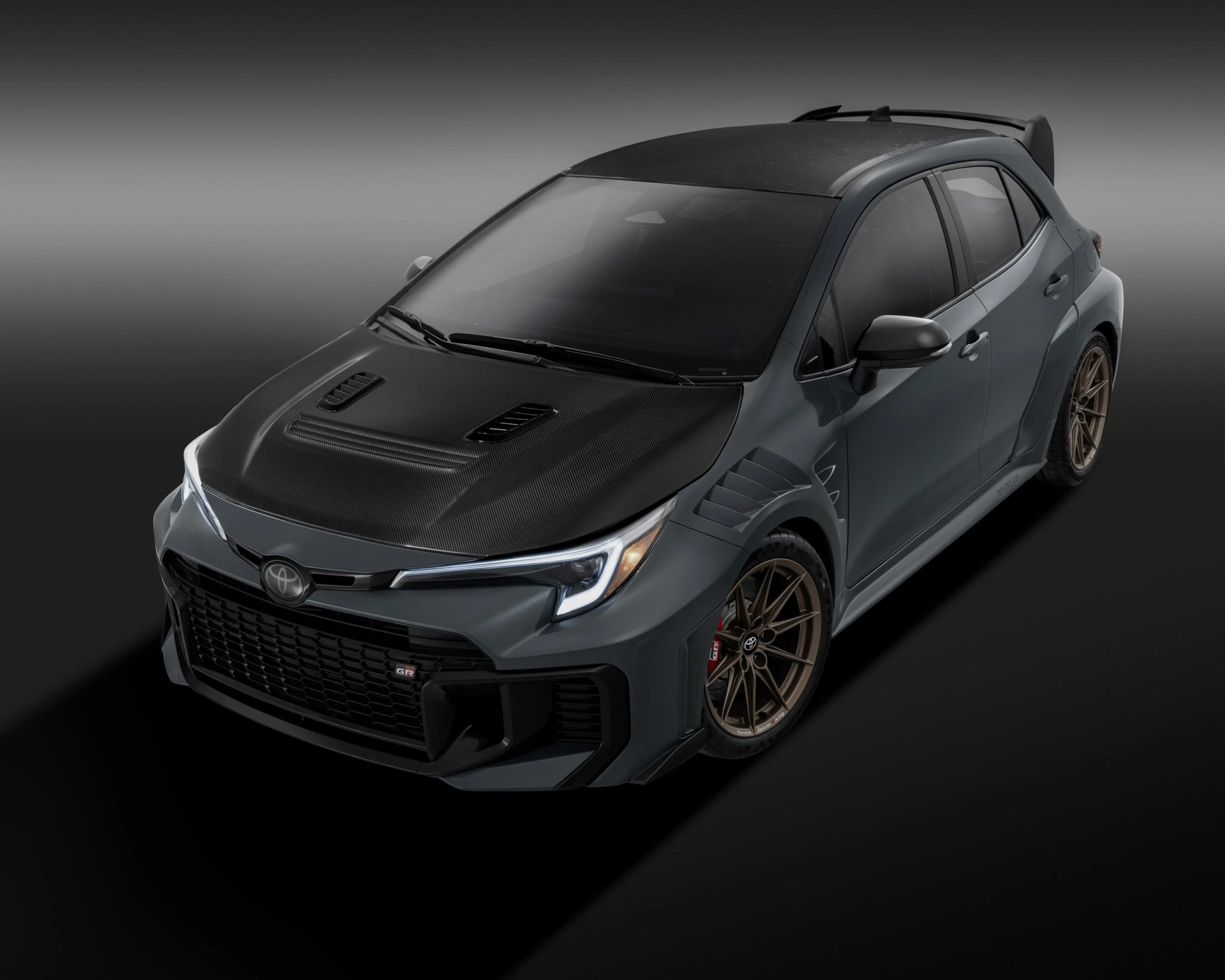 Gray Toyota hatchback with carbon fiber hood and roof, bronze wheels, and sporty aerodynamic features.