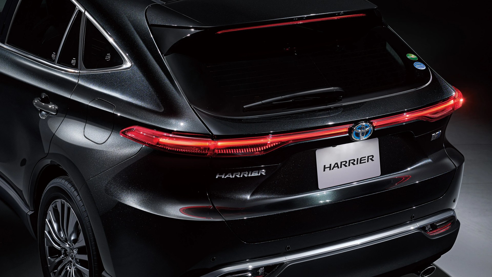 Rear view of a black Toyota Harrier SUV with illuminated taillights and a rear windshield wiper.