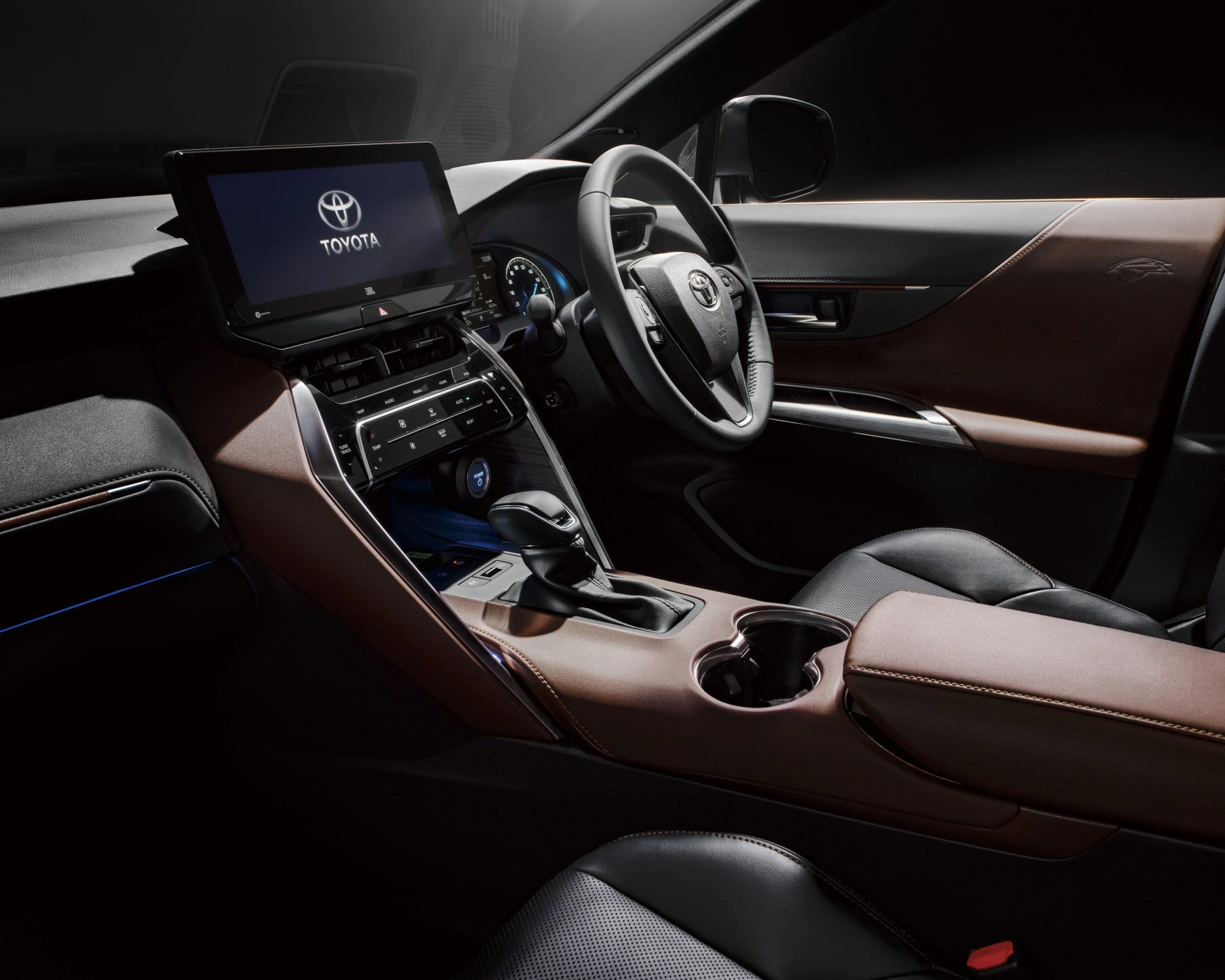 Toyota car interior with black leather steering wheel, touchscreen display, and brown leather-trimmed dashboard and door panel.