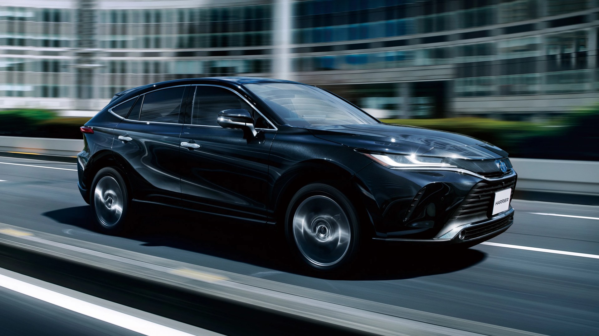 Black Toyota Harrier SUV driving on a city street with motion blur on wheels and background.